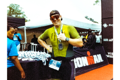 A triathlete stands at the finish line with their medal.